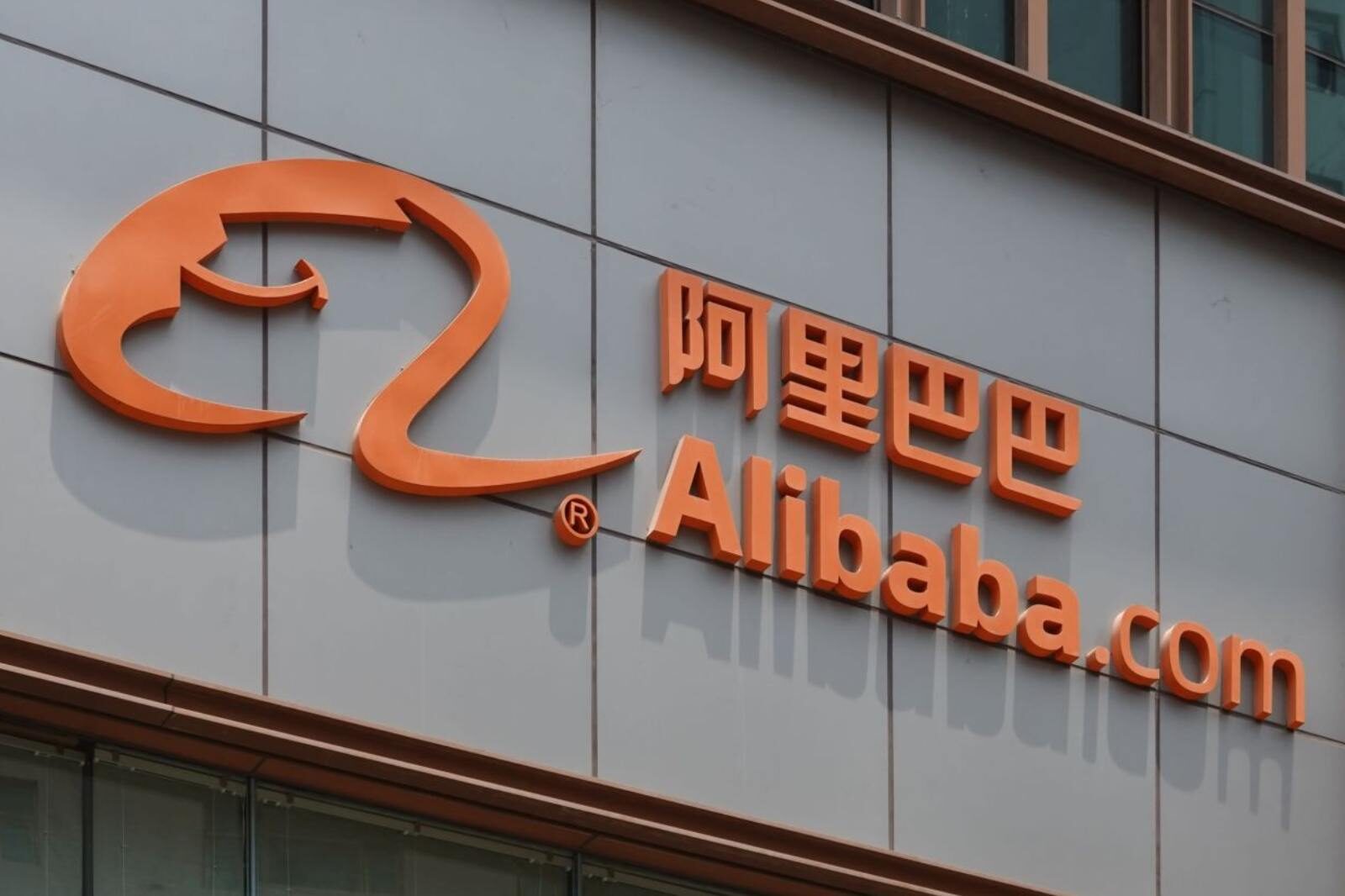 Orange Alibaba.com logo with Chinese characters on a gray building facade. The bold colors convey a modern, corporate tone.